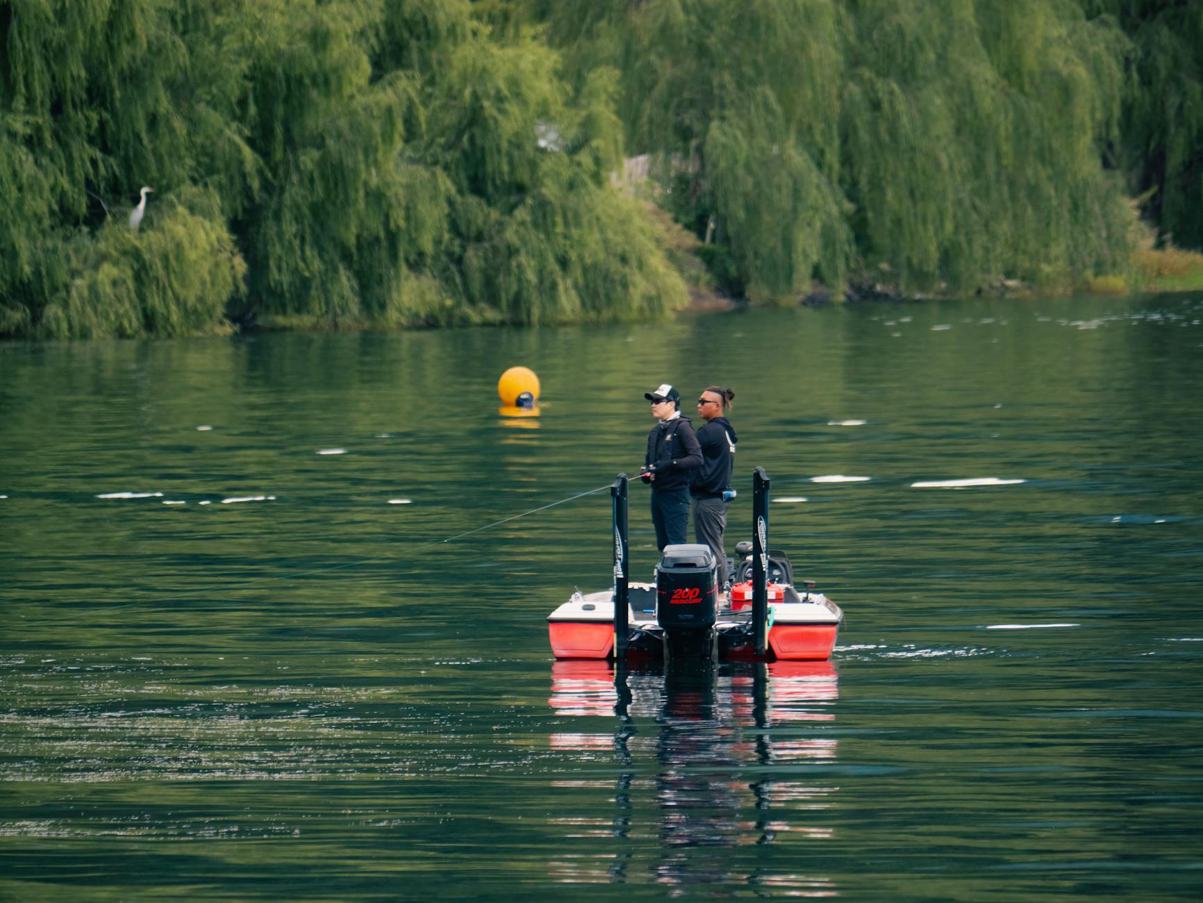 Dwóch wędkarzy łowi z łodzi na spokojnym jeziorze otoczonym zielenią
