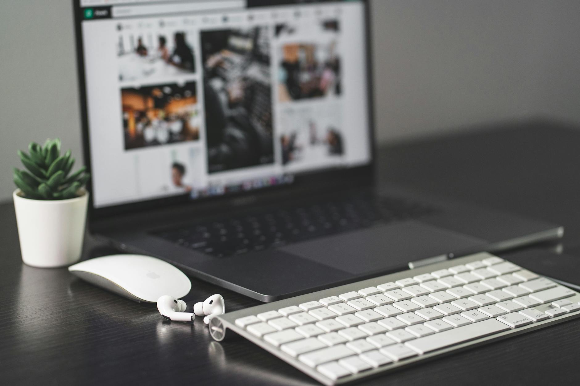 Nowoczesne biurko z laptopem, klawiaturą, myszką, AirPods i małą rośliną