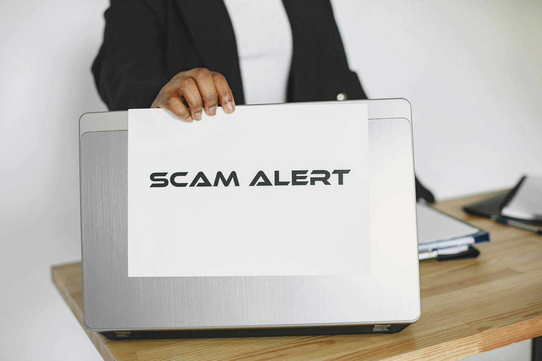 Osoba trzyma kartkę Scam Alert nad laptopem, ostrzegając przed oszustwem online