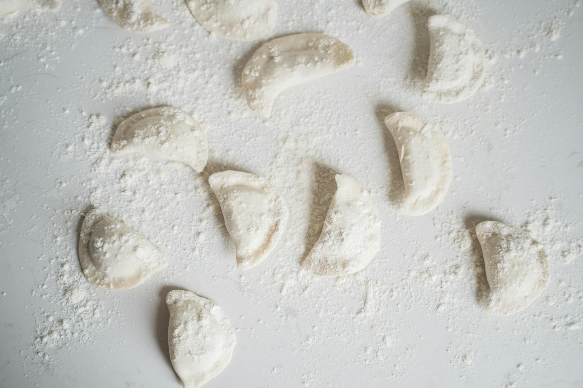 Surowe domowe pierogi ułożone na oprószonym mąką blacie