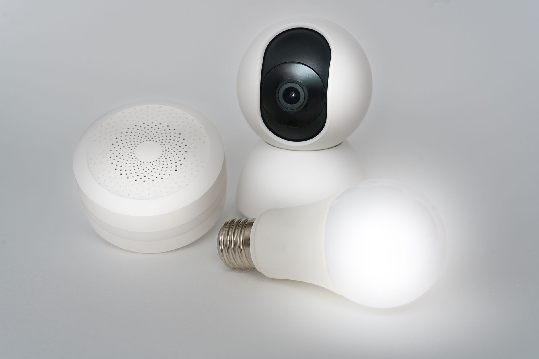Zestaw urządzeń smart home: kamera, głośnik i żarówka na białym tle