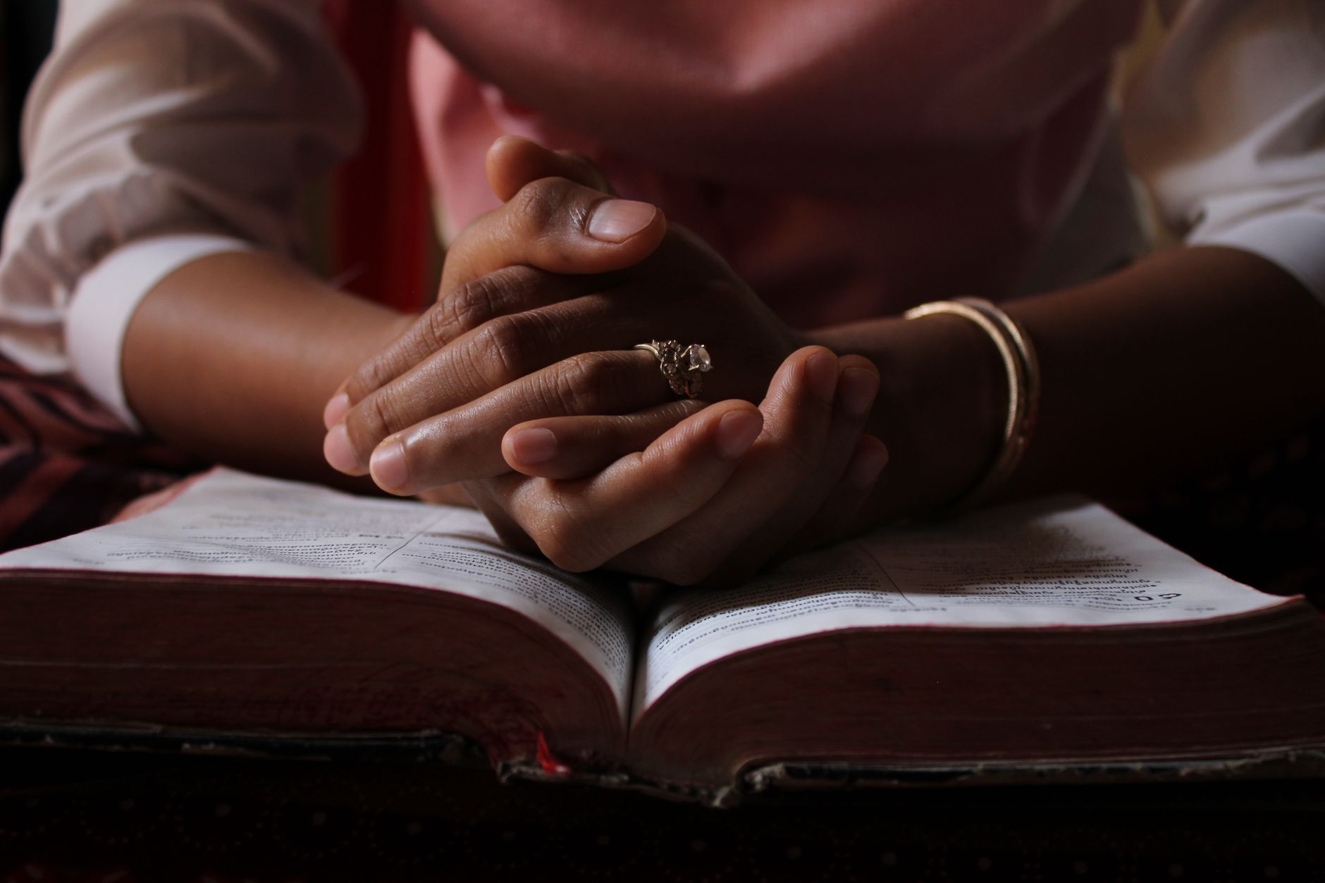 Złożone dłonie do modlitwy nad otwartą Biblią podczas osobistej lektury